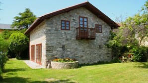 A stone building with a sloped roof, a wooden balcony, and a small garden area. - La Regalina (Valdes)
