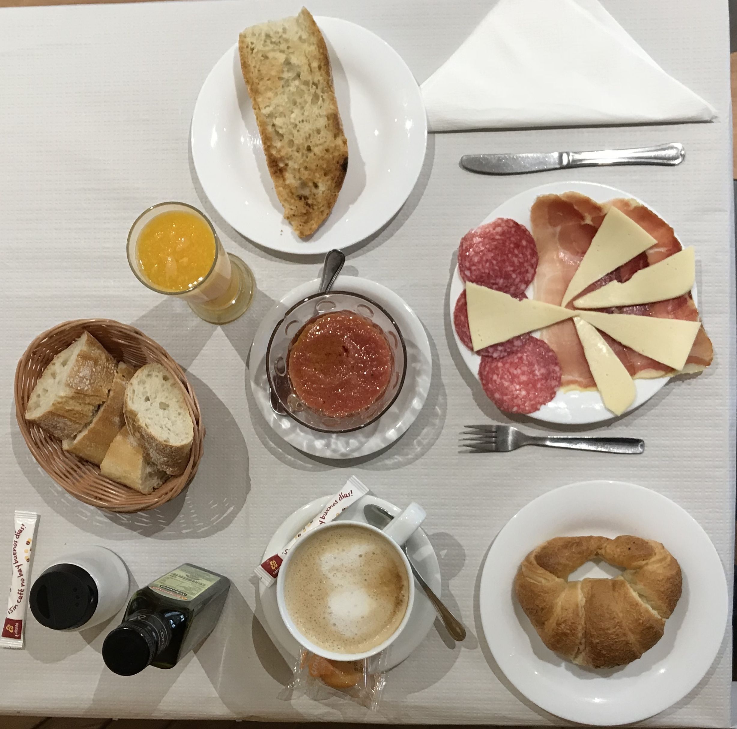 A breakfast table with bread, cheese, salami, jam, coffee, and a croissant.