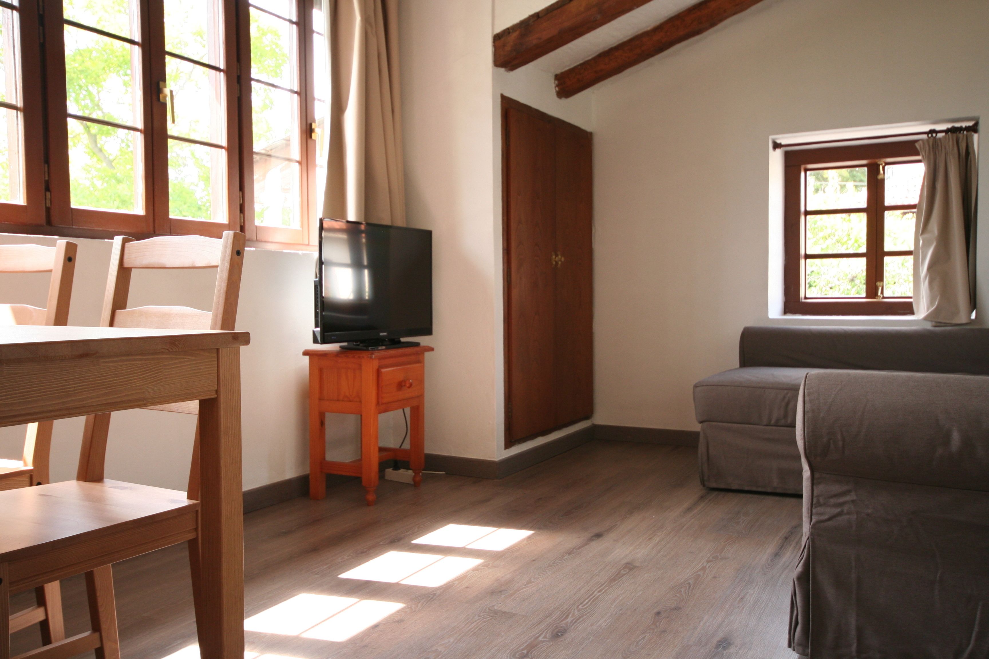 A room with a wooden table, a television on a small stand, a sofa, and a window with curtains.