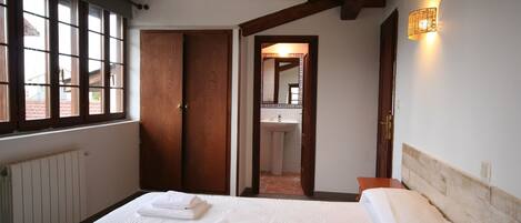 Un dormitorio con cama, ventana, puerta y baño visible a través de una puerta abierta.