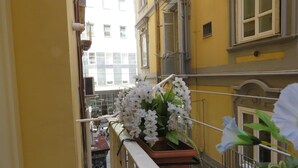 A balcony with a potted white flower arrangement, a metal railing, and a view of a yellow building with multiple windows. - Olimpo degli Dei (Naples)