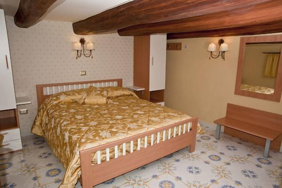 A bedroom with a wooden bed, two bedside tables, a bench, and a mirror on the wall.