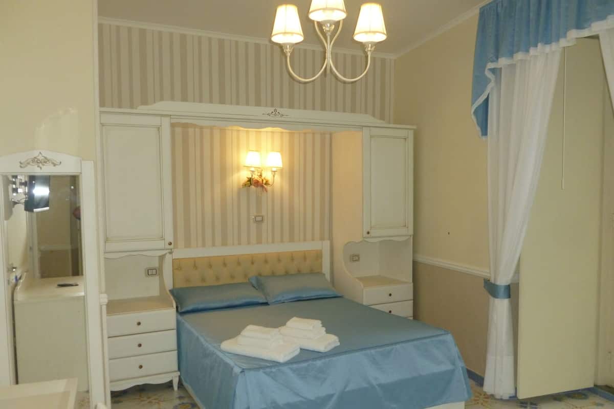 A bedroom with a bed, bedside tables, a mirror, and a chandelier.