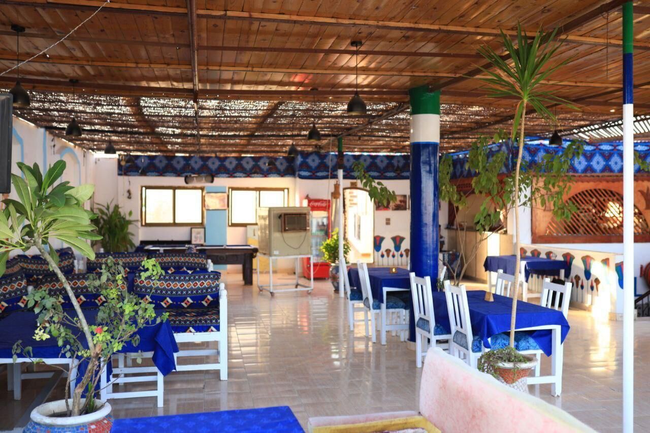 Een restaurant met een hoge plafond en houten balken, met tafels en stoelen met blauwe tafelkleden, en potplanten.