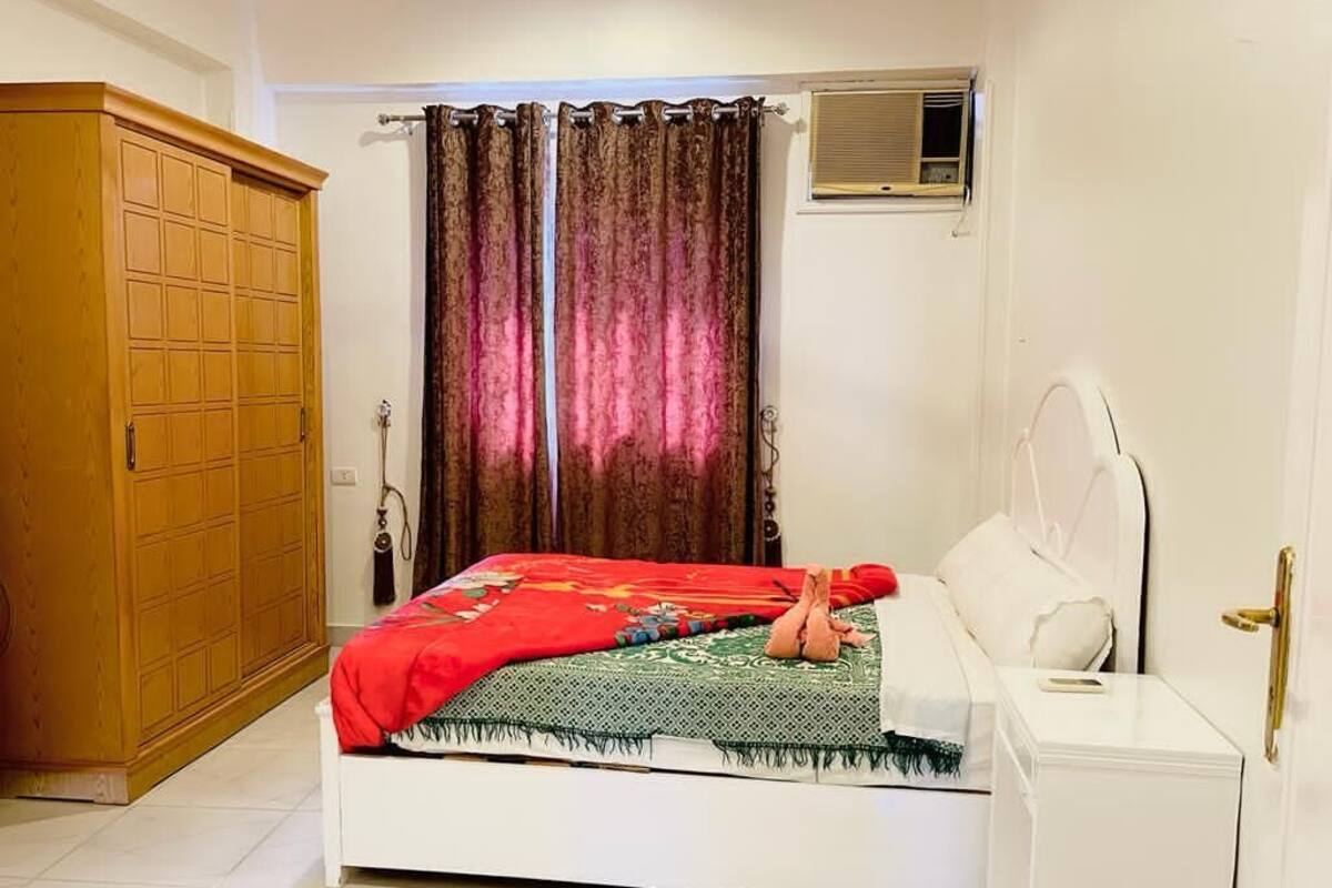 A bedroom with a bed, a wardrobe, a bedside table, and a window with curtains.