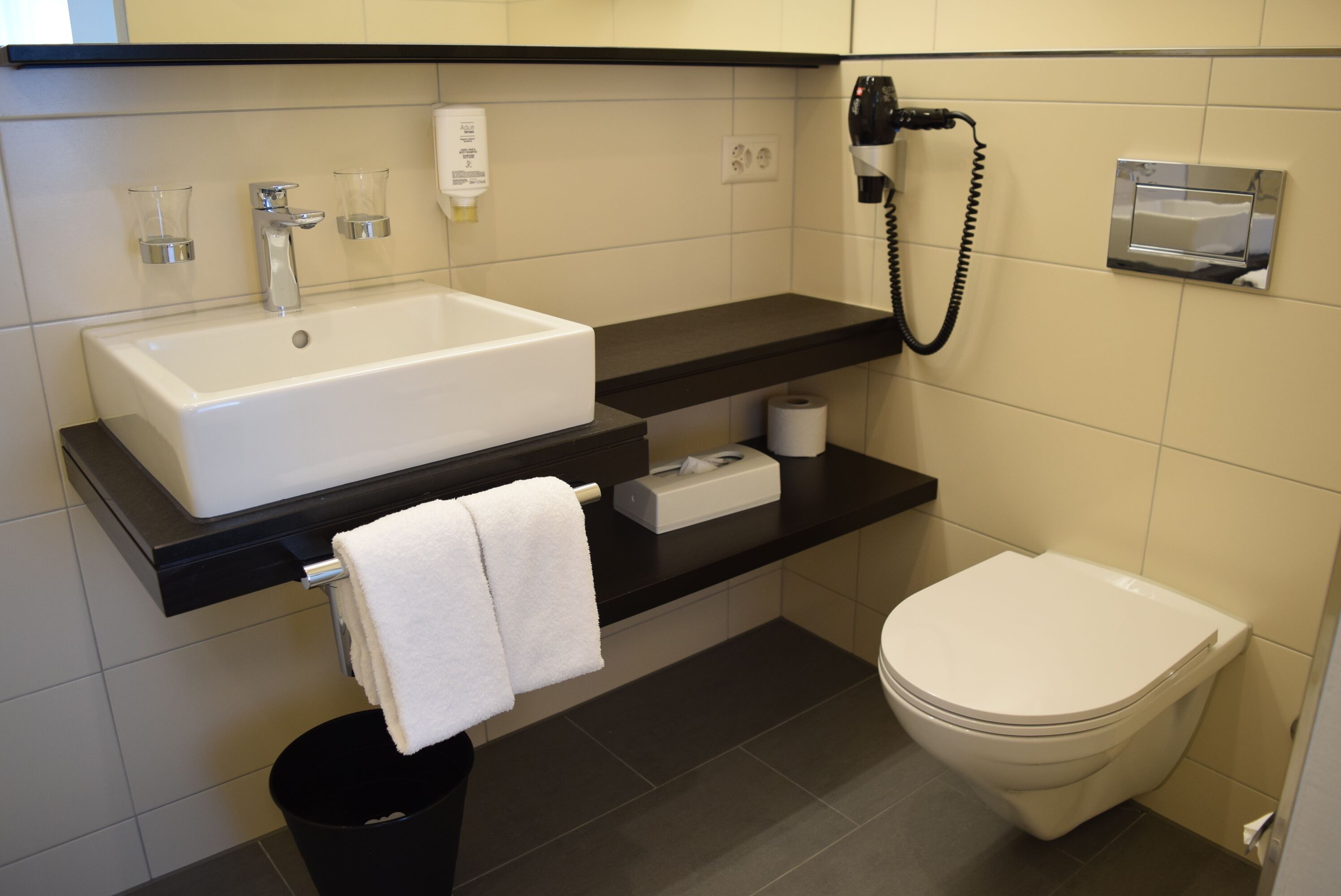A bathroom with a sink, toilet, and a hairdryer mounted on the wall.
