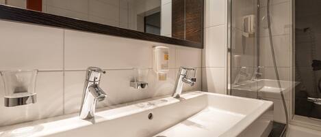 Un baño moderno con un lavamanos grande blanco, dos grifos de cromo y una zona de ducha con mampara de vidrio.