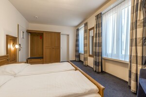 Habitación de hotel con dos camas, armario de madera y ventana con cortinas.