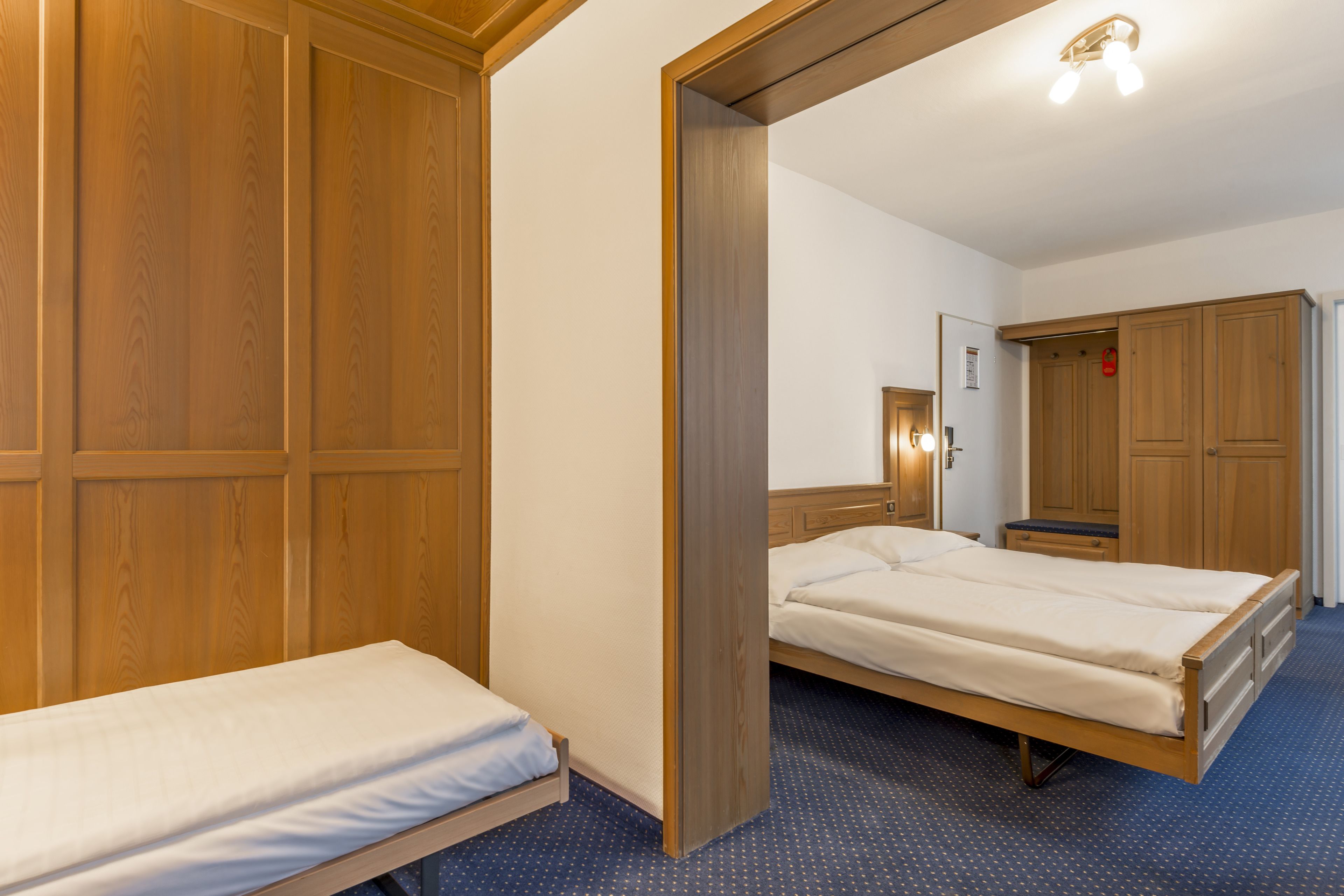 A hotel room with two single beds, wooden wardrobes, and a mirror.