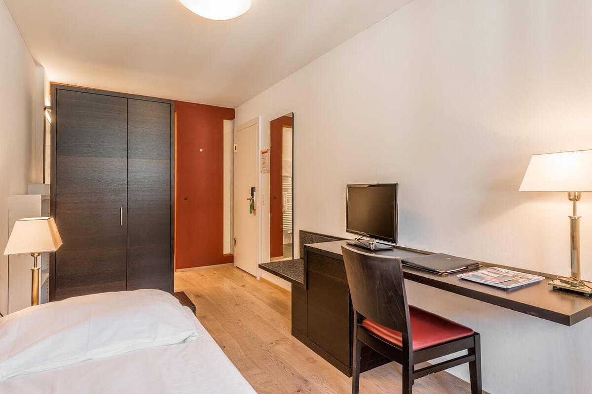 A hotel room with a bed, a desk with a computer, a chair, and a TV.