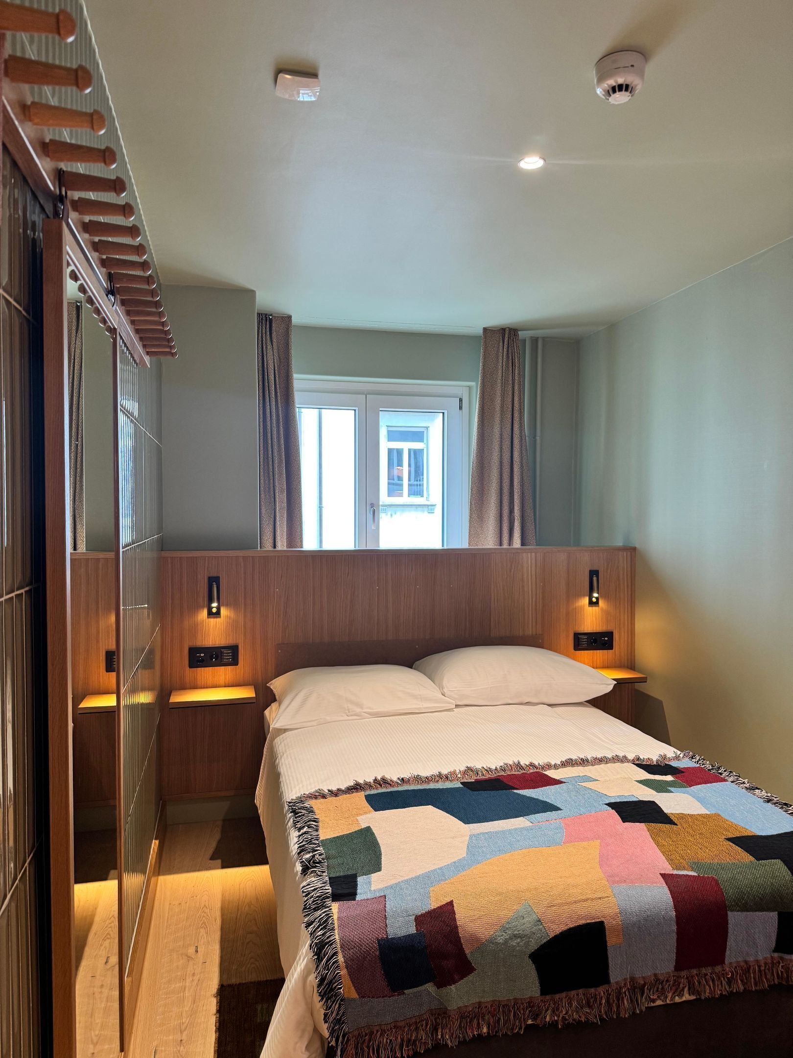 A bedroom with a bed, two bedside lamps, a window, and a wardrobe.