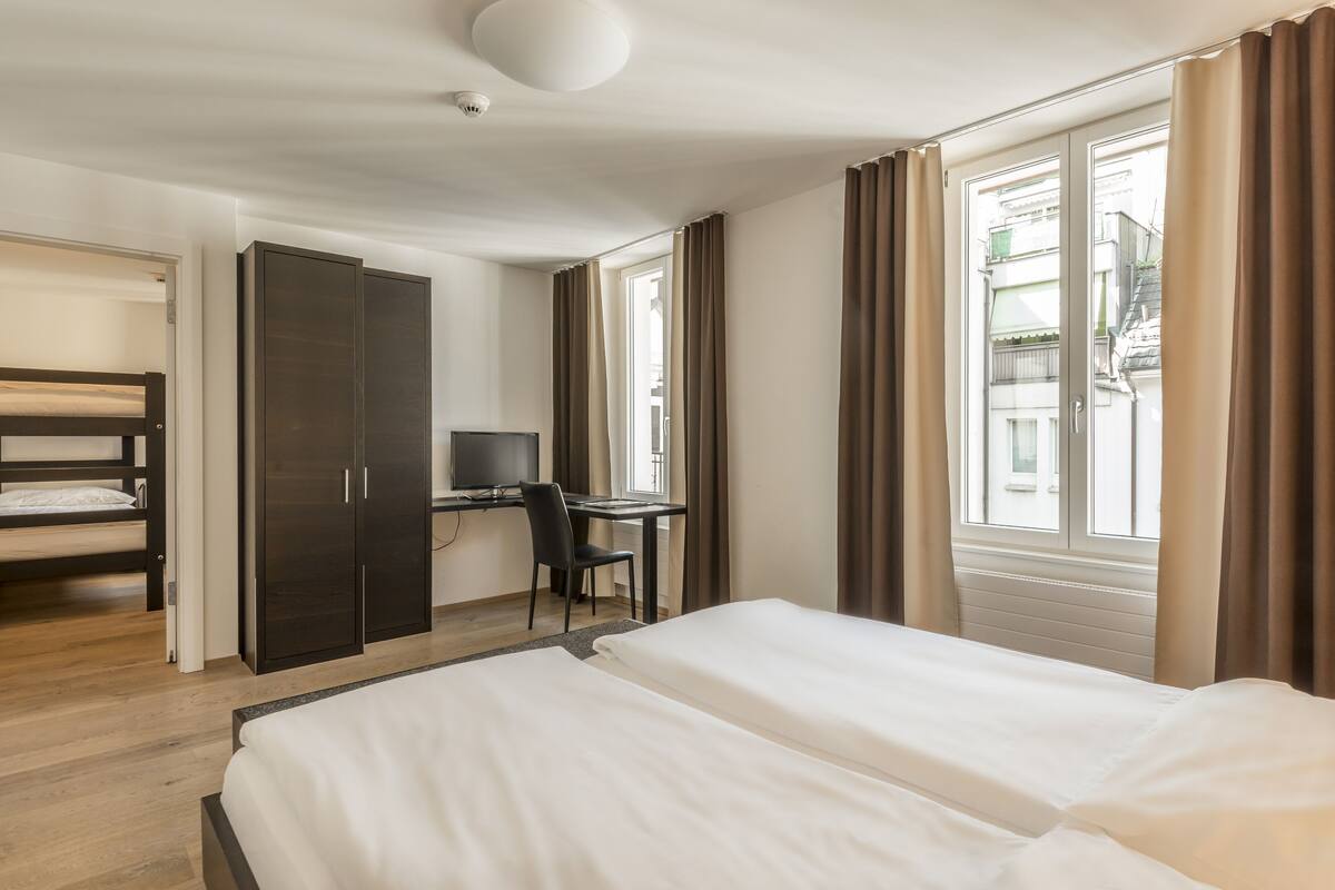 A hotel room with a double bed, a desk with a chair, a wardrobe, and a television.