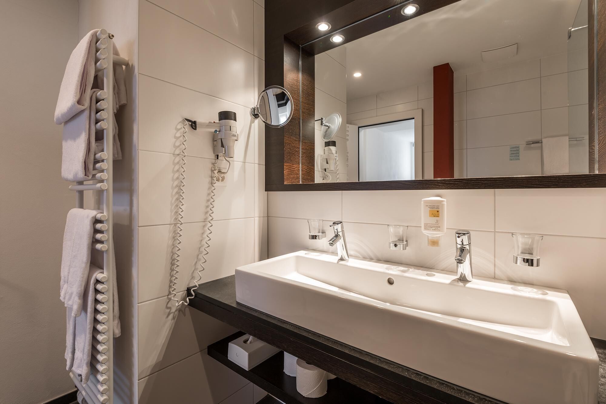 Un baño moderno con un lavabo blanco, un espejo y un perchero para toallas.