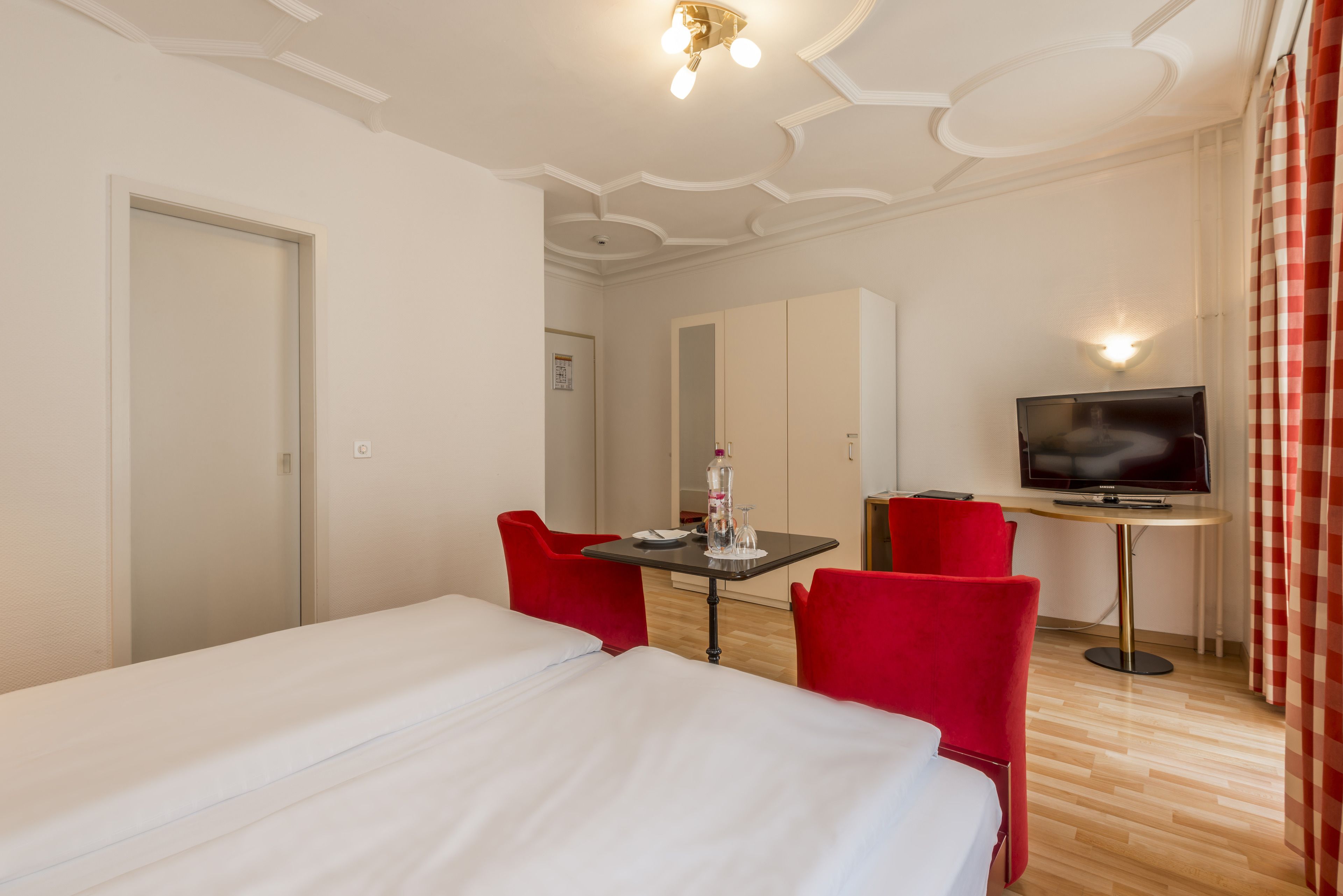 Ein Hotelzimmer mit einem Bett, einem Schreibtisch mit Stuhl, einem Fernseher und einem Spiegel.