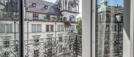 A balcony with ornate wrought iron railings overlooking a historic building with a tiled roof and a green dome.