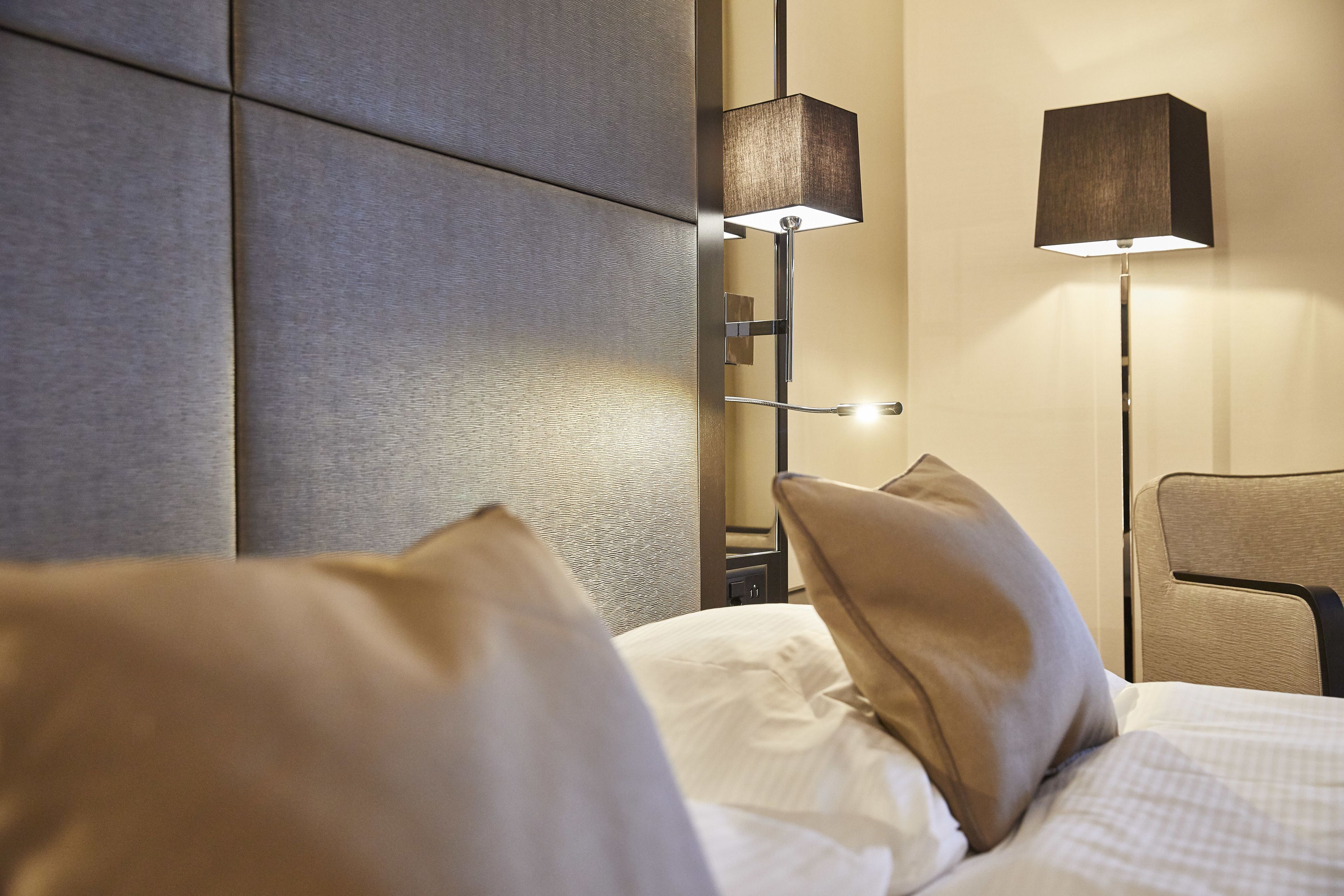 A neatly made bed with pillows, a wall-mounted lamp, and a chair in a hotel room.