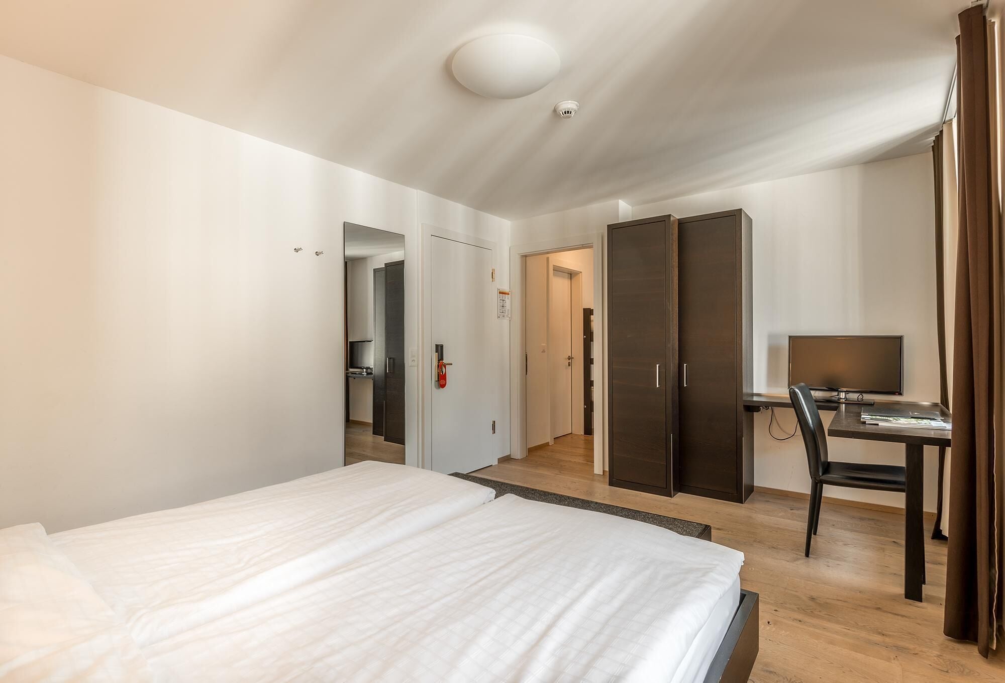 Habitación de hotel con una cama grande, un escritorio con una silla, un televisor y un armario.