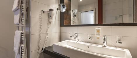 A modern bathroom with a white sink, two faucets, a mirror, and a towel rack with towels.
