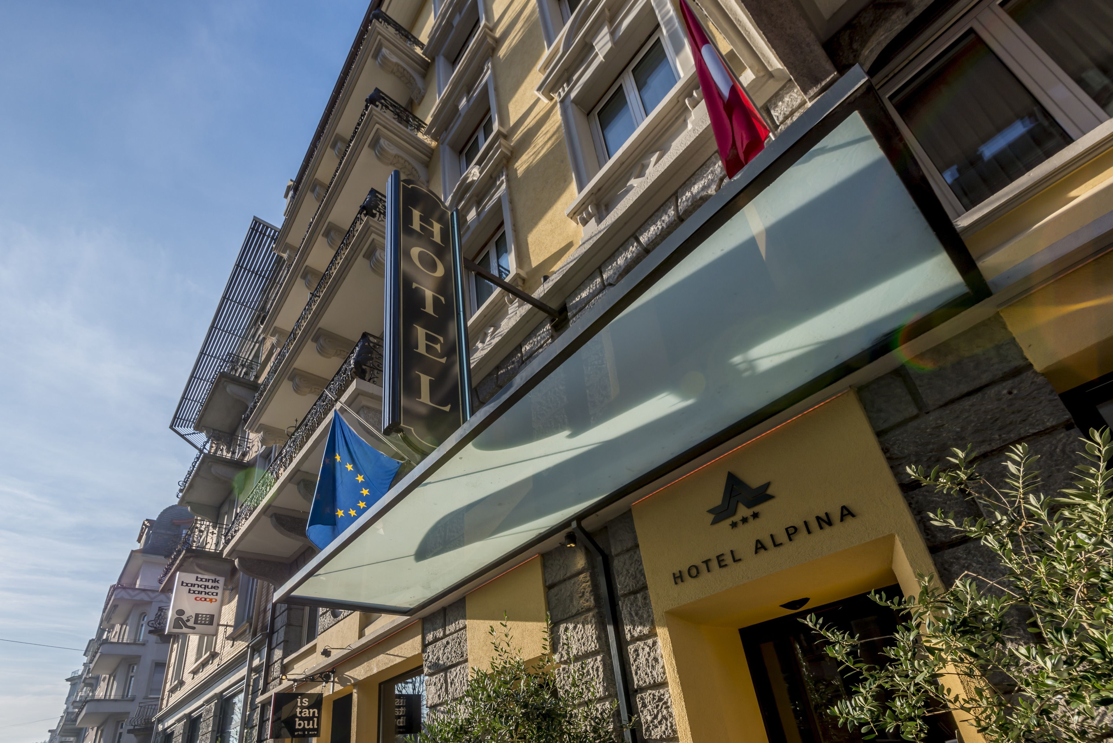A hotel with a sign reading "HOTEL ALPINA" and a European Union flag.