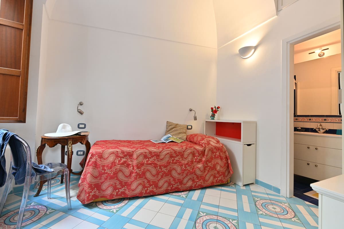 Ein kleines, gemütliches Schlafzimmer mit einem Einzelbett, einem kleinen Tisch, einem Stuhl und einem Kleiderschrank.