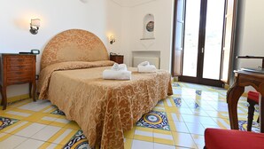 A hotel room with a bed, two bedside tables, a red chair, a window with a view, and a tiled floor. - Hotel Croce di Amalfi (Amalfi)