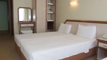Una cama doble con ropa de cama blanca, un cabecero de madera, una mesita de noche con teléfono, un espejo y un armario con estantes.