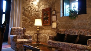Un salón acogedor con pared de piedra, un sofá estampado con motivos florales, una mesa de centro de madera y una lámpara.