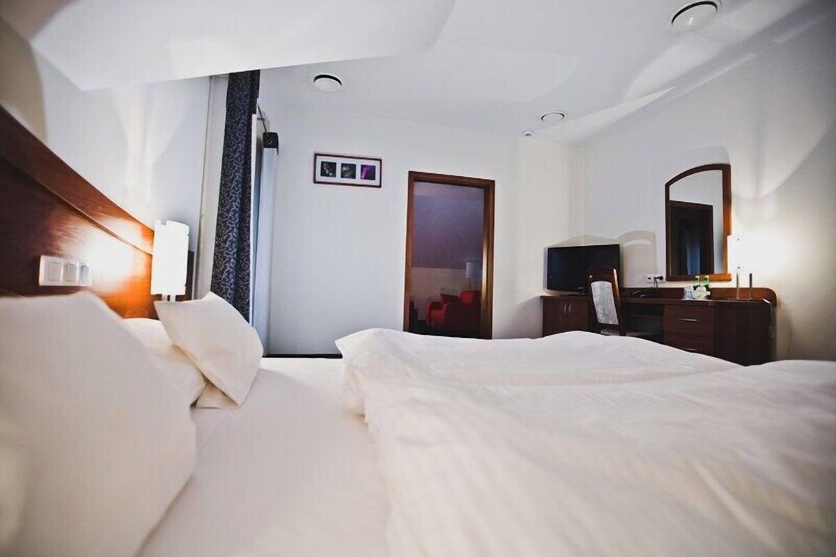 A hotel room with a bed, a desk, a chair, a TV, and a door.