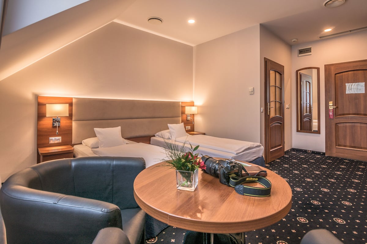 A hotel room with a bed, a desk with a camera, a chair, and a small table with a vase of flowers.