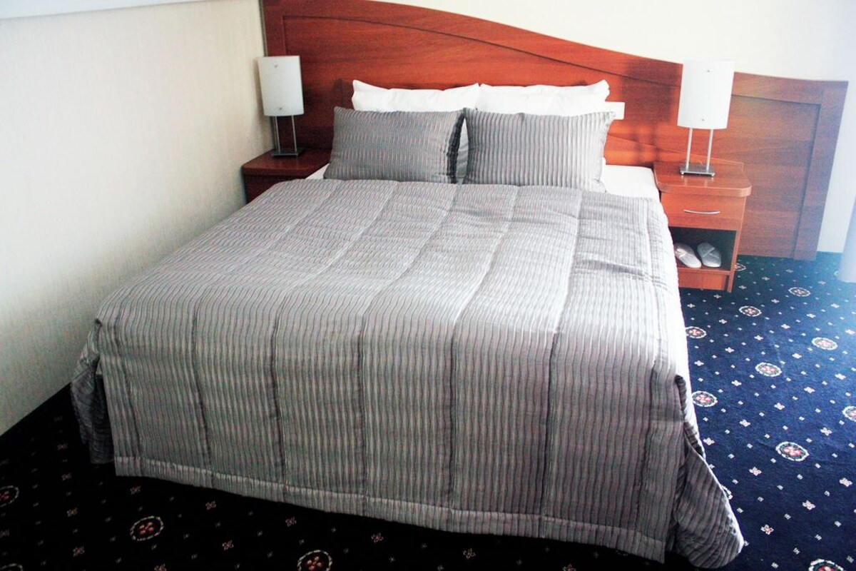 A neatly made bed with a striped bedspread, two bedside tables with lamps, and a patterned carpet.