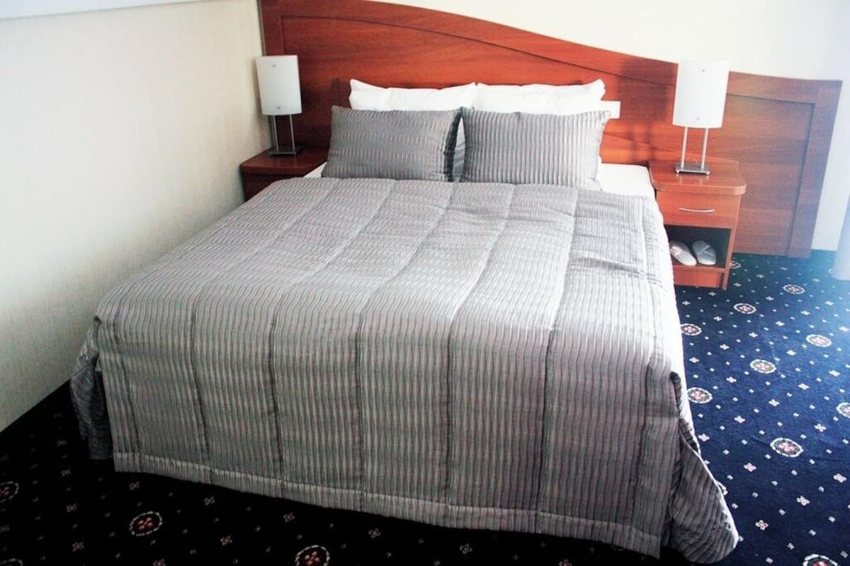 A neatly made bed with a striped bedspread, two bedside tables with lamps, and a patterned carpet.