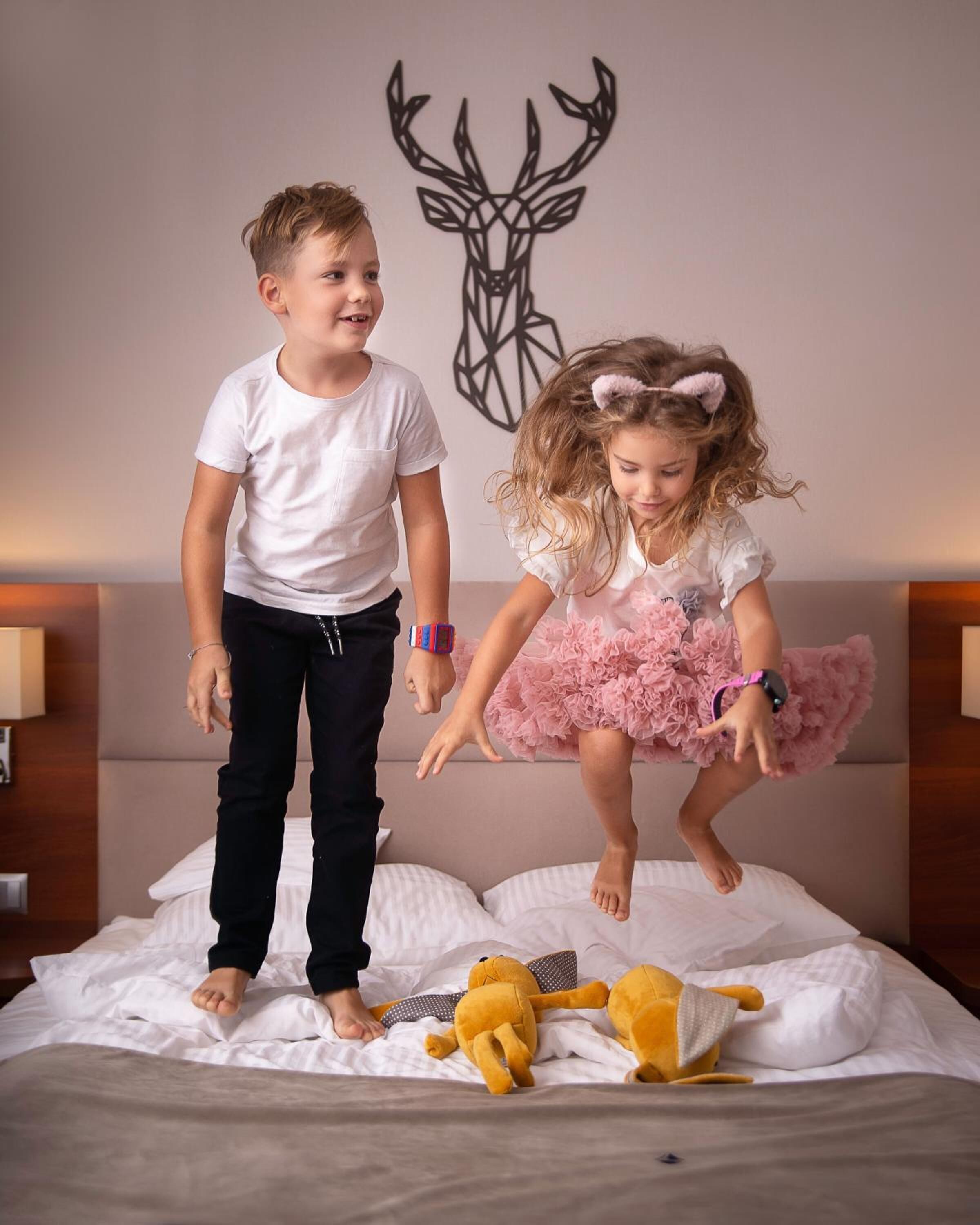 Two children jumping on a bed with a stuffed toy.
