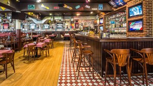 Un bar con suelo a cuadros, sillas de madera y barra con varios televisores.