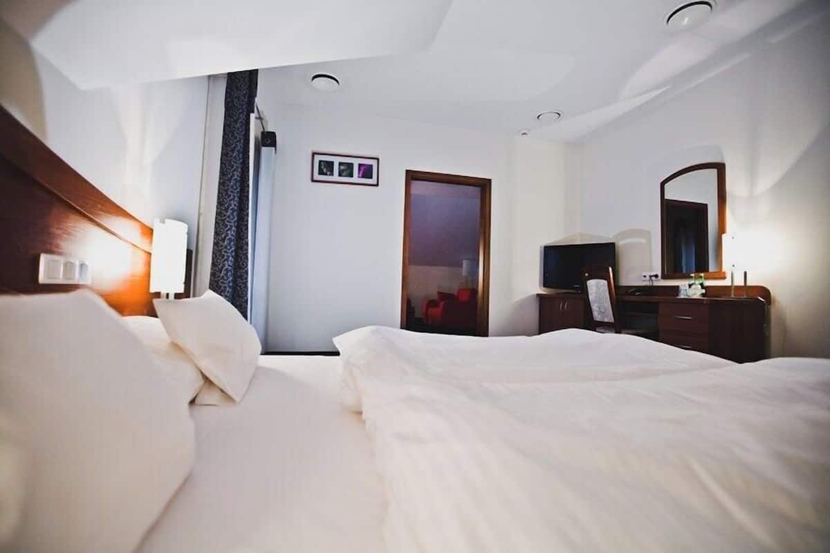 A hotel room with a bed, a desk, a chair, a TV, and a door.