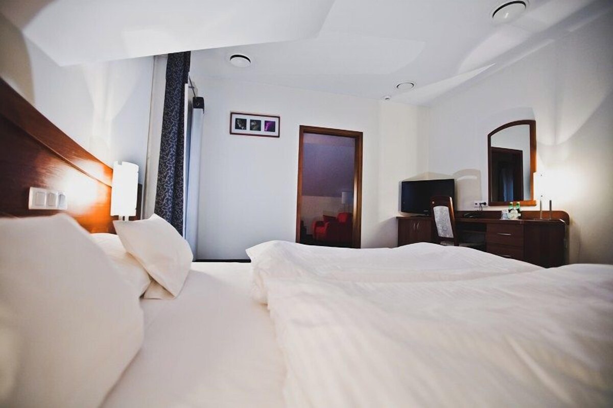 A hotel room with a bed, a desk, a chair, a TV, and a door.