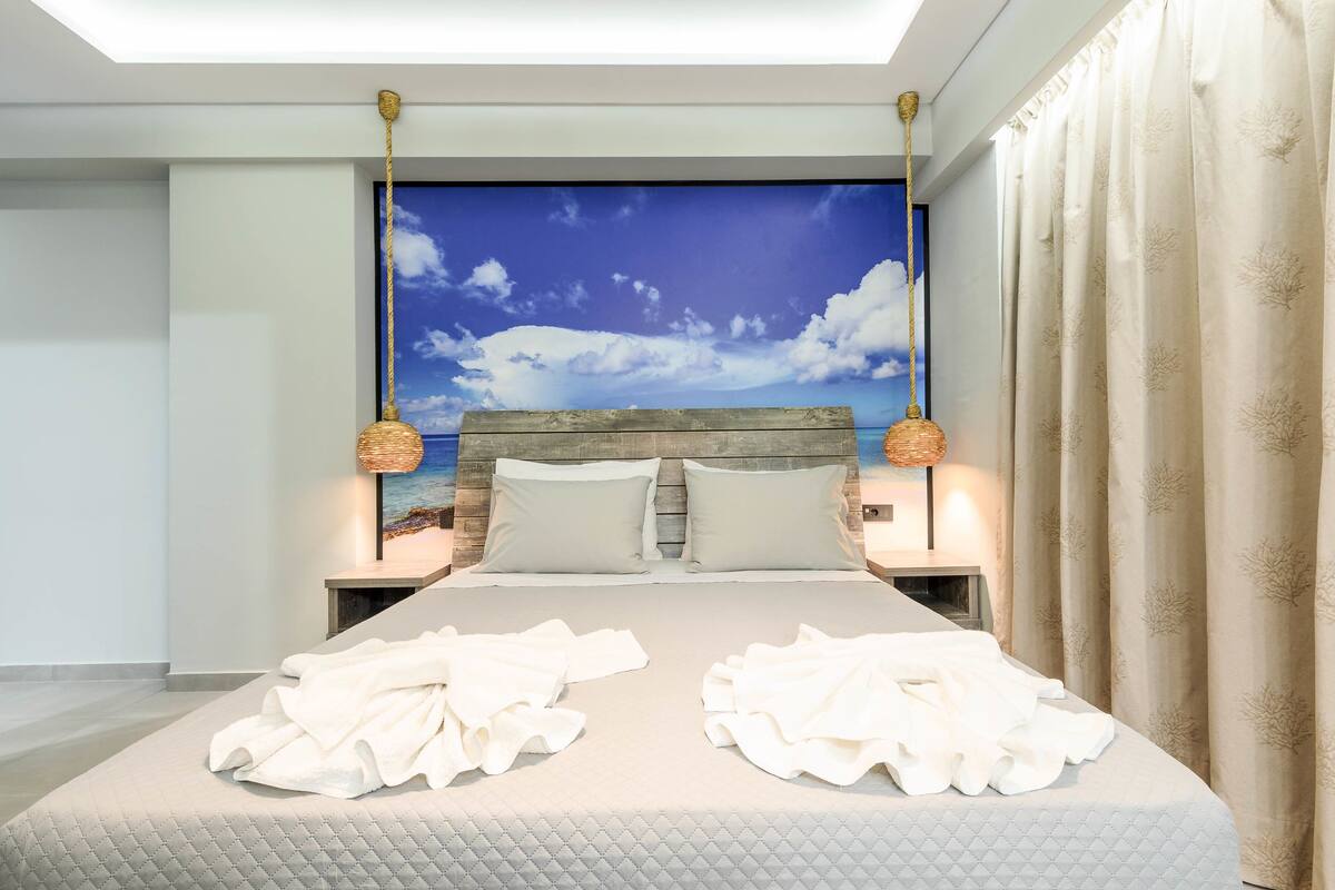 Ein modernes Hotelzimmer mit einem großen Bett, zwei Nachttischen und Meerblick durch ein großes Fenster.