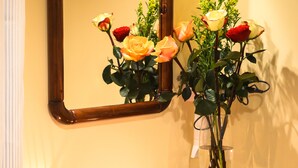 Eine hölzerne Kommode mit Spiegel darüber, eine Vase mit Rosen und verstreute Rosenblätter auf der Kommode.