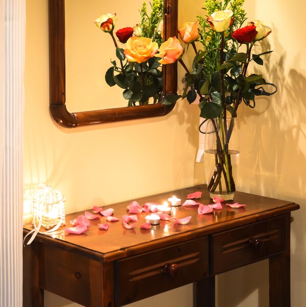 Une commode en bois avec un miroir au-dessus, un vase rempli de roses et des pétales de roses éparpillés sur le dessus de la commode.