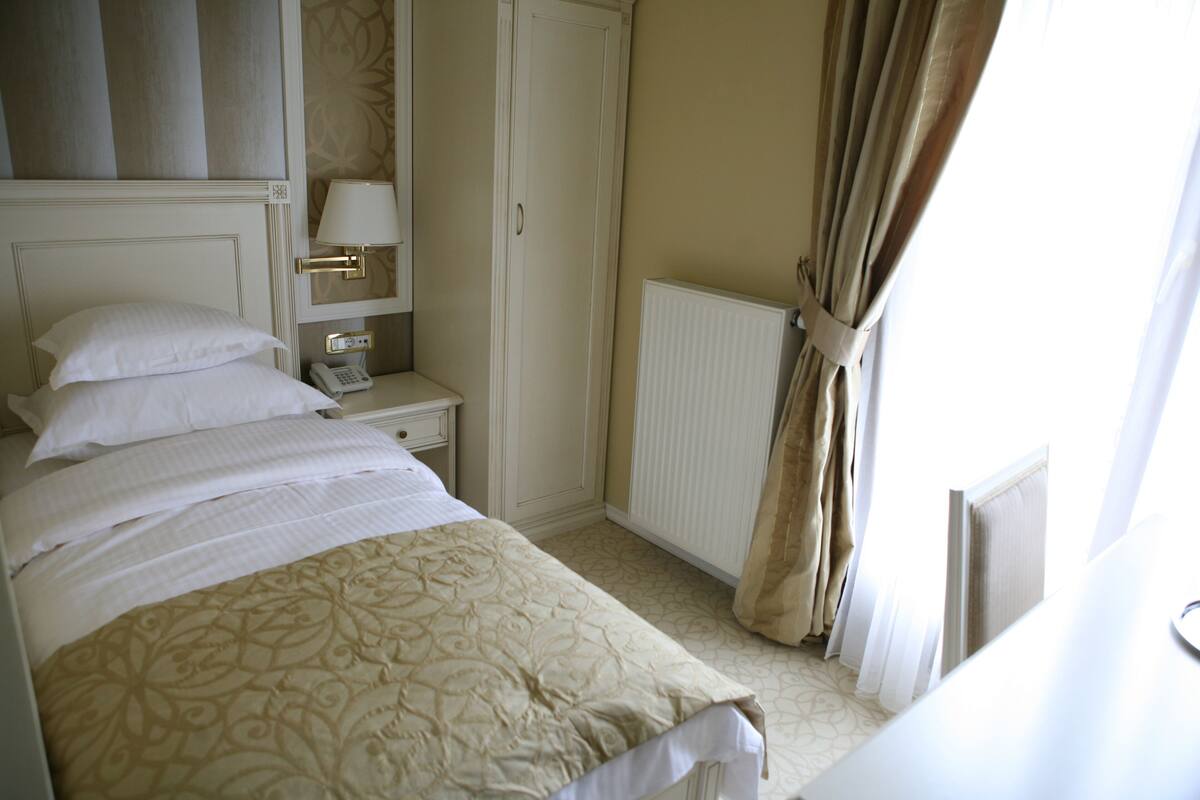 A hotel room with a bed, a nightstand with a lamp, a telephone, and a radiator.