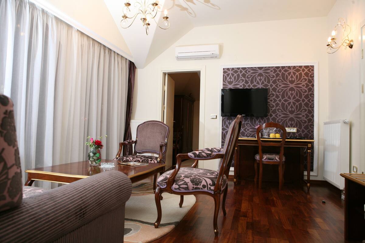 A living room with a sofa, two patterned chairs, a wooden coffee table, and a TV mounted on a patterned wall.