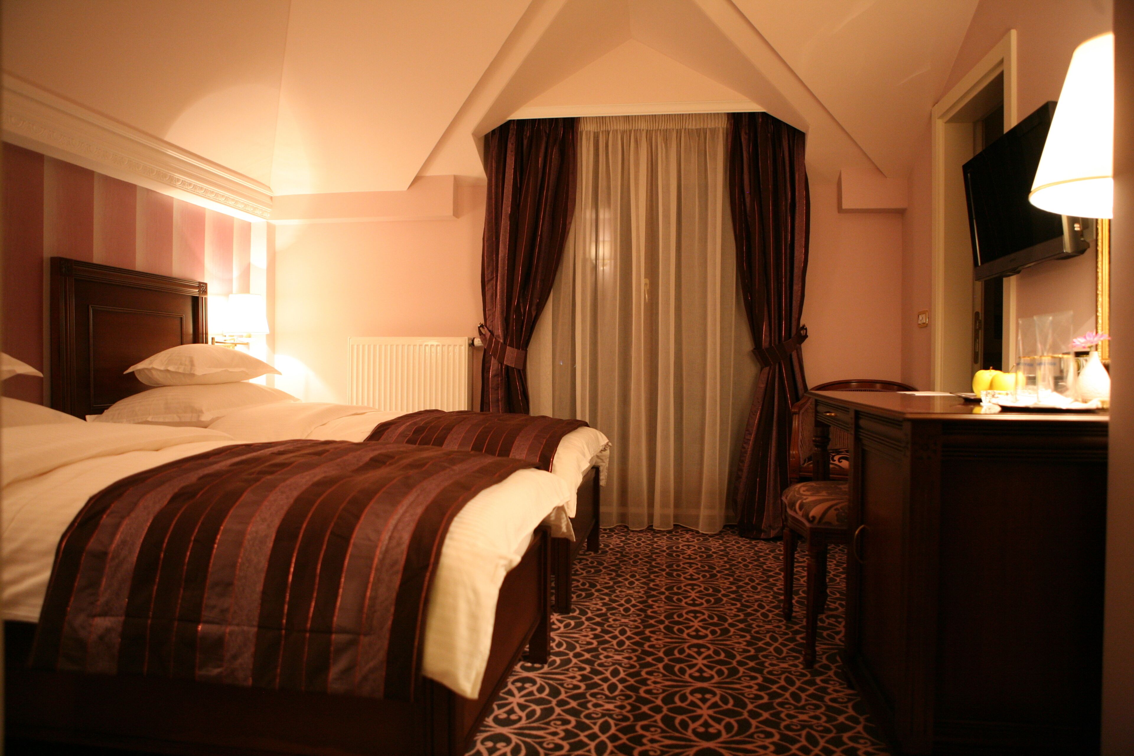 A hotel room with two beds, a desk, a chair, a television, and a patterned carpet.