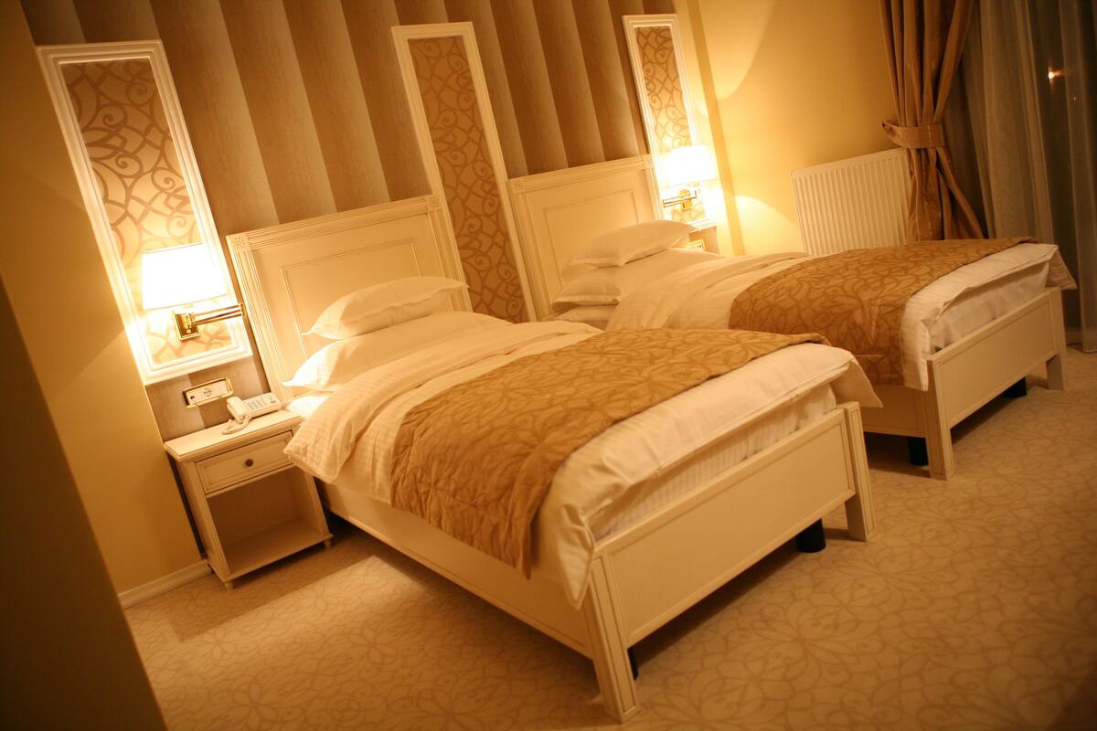 A hotel room with two beds, a nightstand with a phone, and a lamp.