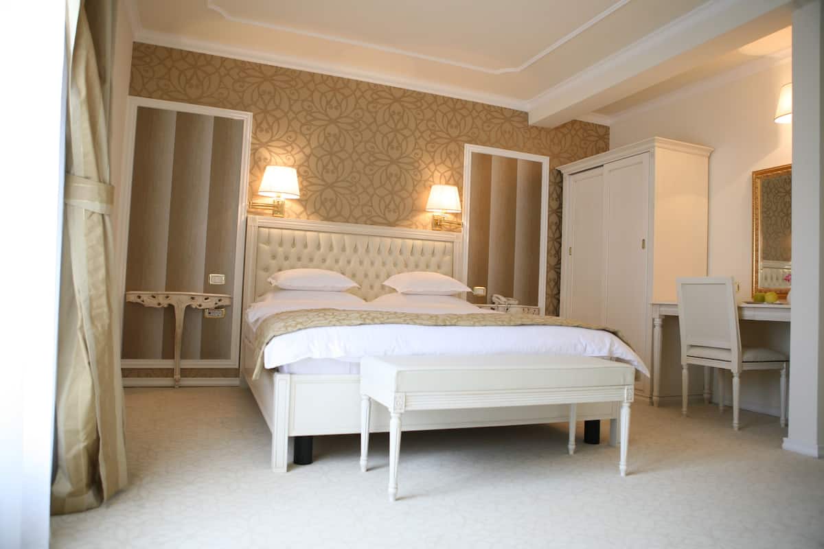 A bedroom with a large bed, two bedside lamps, a chair, a desk, and a wardrobe.