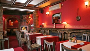 Un restaurante con paredes rojas, arcos de piedra y vigas de madera. Las mesas están dispuestas con manteles blancos y servilletas rojas.