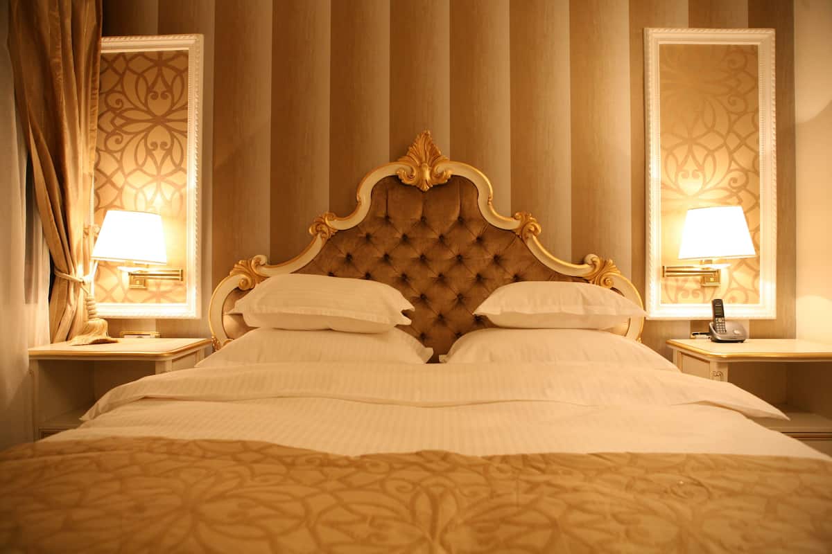 A large bed with a tufted headboard, two bedside tables with lamps, and a mirror on each side.