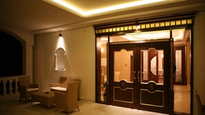 Un vestíbulo de hotel con mostrador de recepción, zona de estar y entrada por un par de puertas.