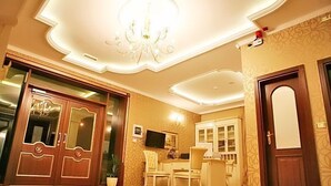 Habitación de hotel con candelabro, zona de comedor con mesa y sillas, y una puerta grande de madera con paneles de vidrio.