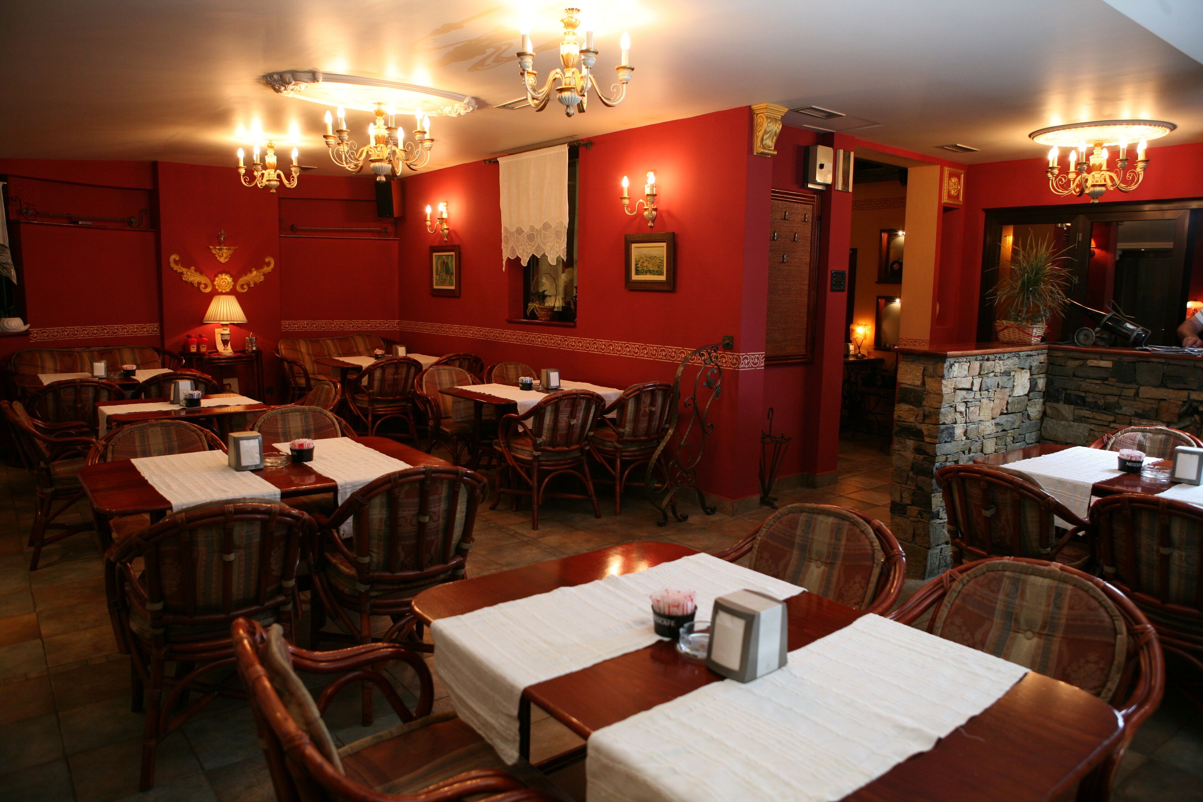 A restaurant with wooden tables and chairs, red walls, and chandeliers.