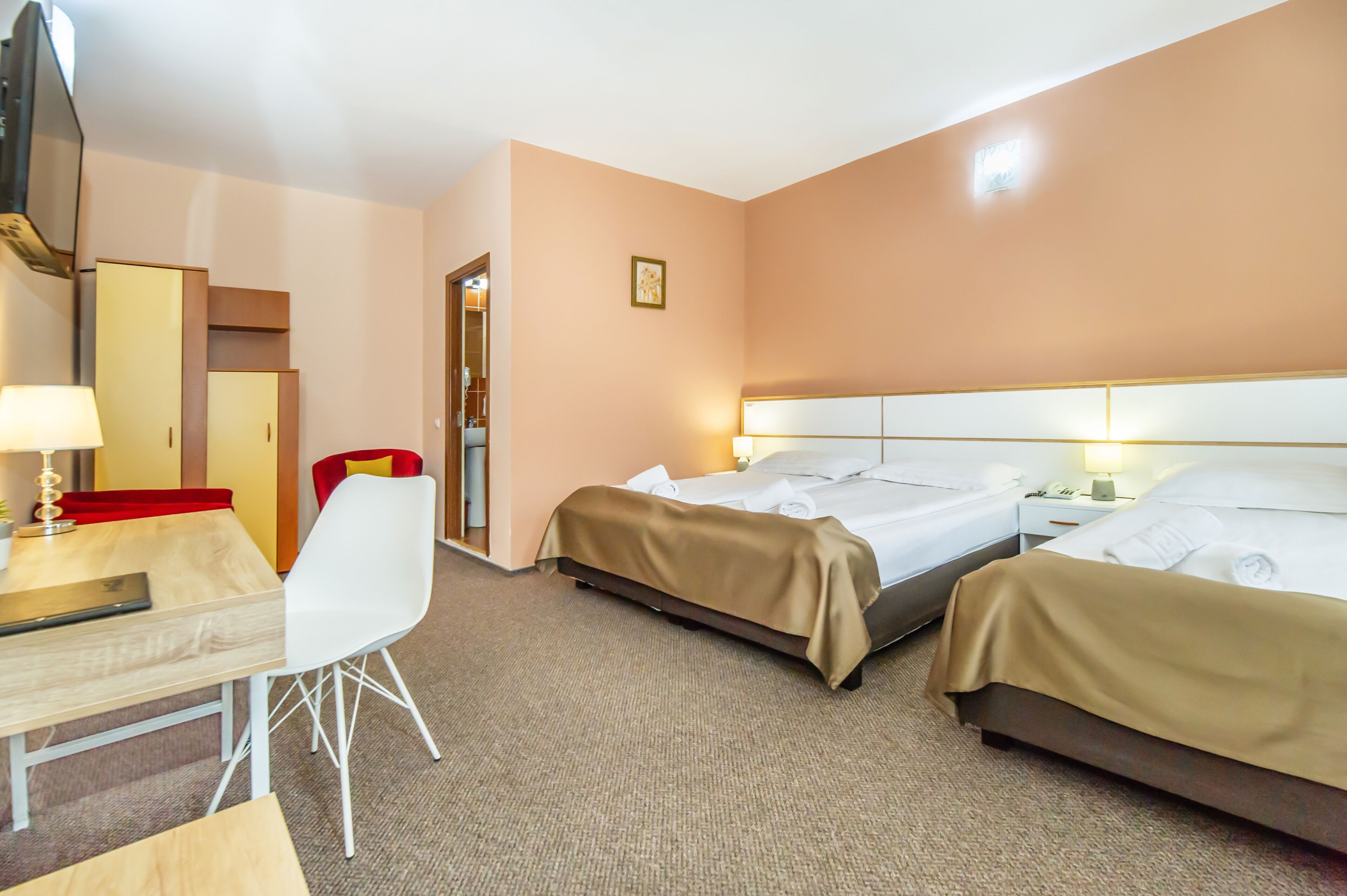 A hotel room with two beds, a desk, a chair, and a TV.
