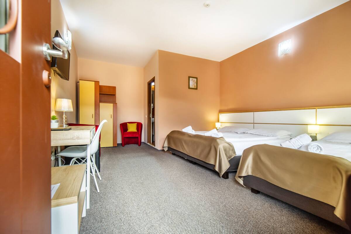 A hotel room with two beds, a desk with a chair, a TV, and a small table with a lamp.